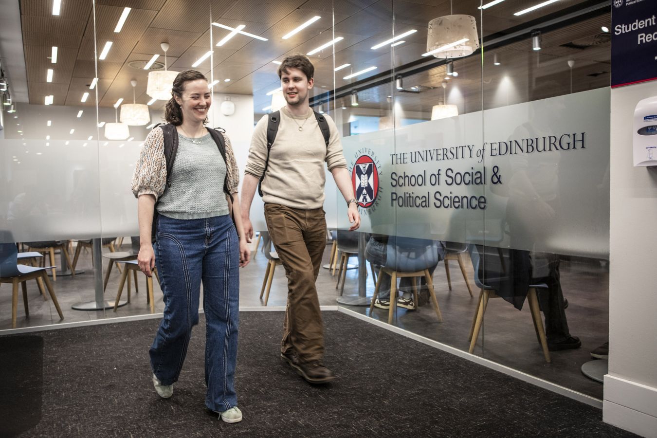 Two students walking in a building, beside a sign for the 'School of Social and Political Science'
