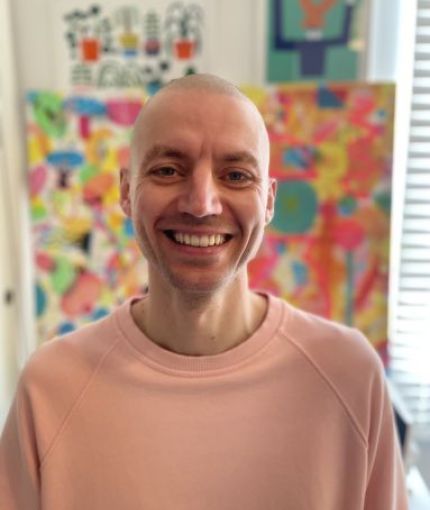 Image of Dan Castro smiling in front of a brightly coloured abstract artistic background