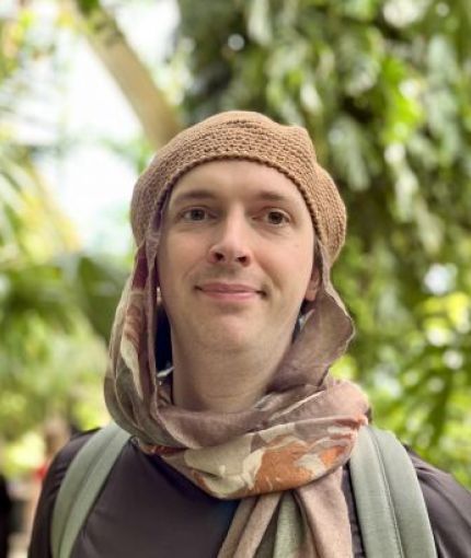 Headshot of Dr Peaks wearing a head scarf and beret against out-of-focus trees in the background