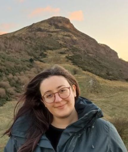 A photo of a woman smiling, standing in front of a hill