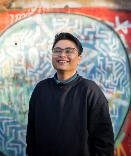 Person in black jumper, short hair, and glasses smiling into the camera