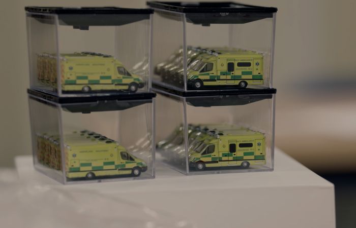 Small model ambulances are stacked on top of each other inside four plastic sealed boxes. They sit on top a white table. 