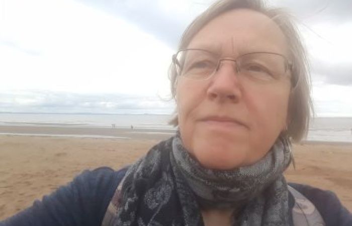 Jackie Gulland looking into the distance, behind is a sandy beach