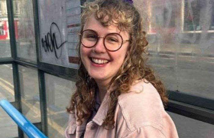 A picture of a woman with curly hair, she is smiling and wearing a pink jacket.
